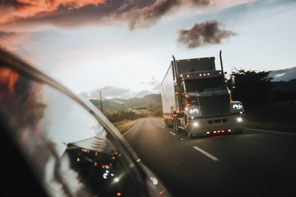View from a truck cab: a semi with its lights on coming down a two-lane highway at dusk
