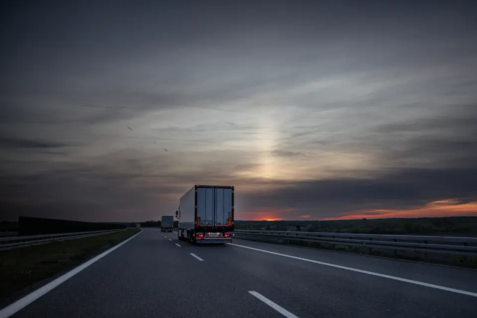 A tractor-trailer on an empty highway at sunset